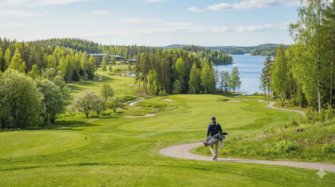 Golfaaja kävelee Vierumäen vehreällä ja kumpuilevalla golfkentällä keväällä, taustallaan kaunis suomalainen järvimaisema ja metsä.